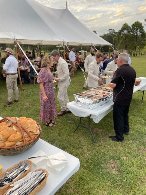 A Group Of People Are Standing Around A Table With Food In Front Of A Tent — Tru Blu Catering In Wauchope, NSW