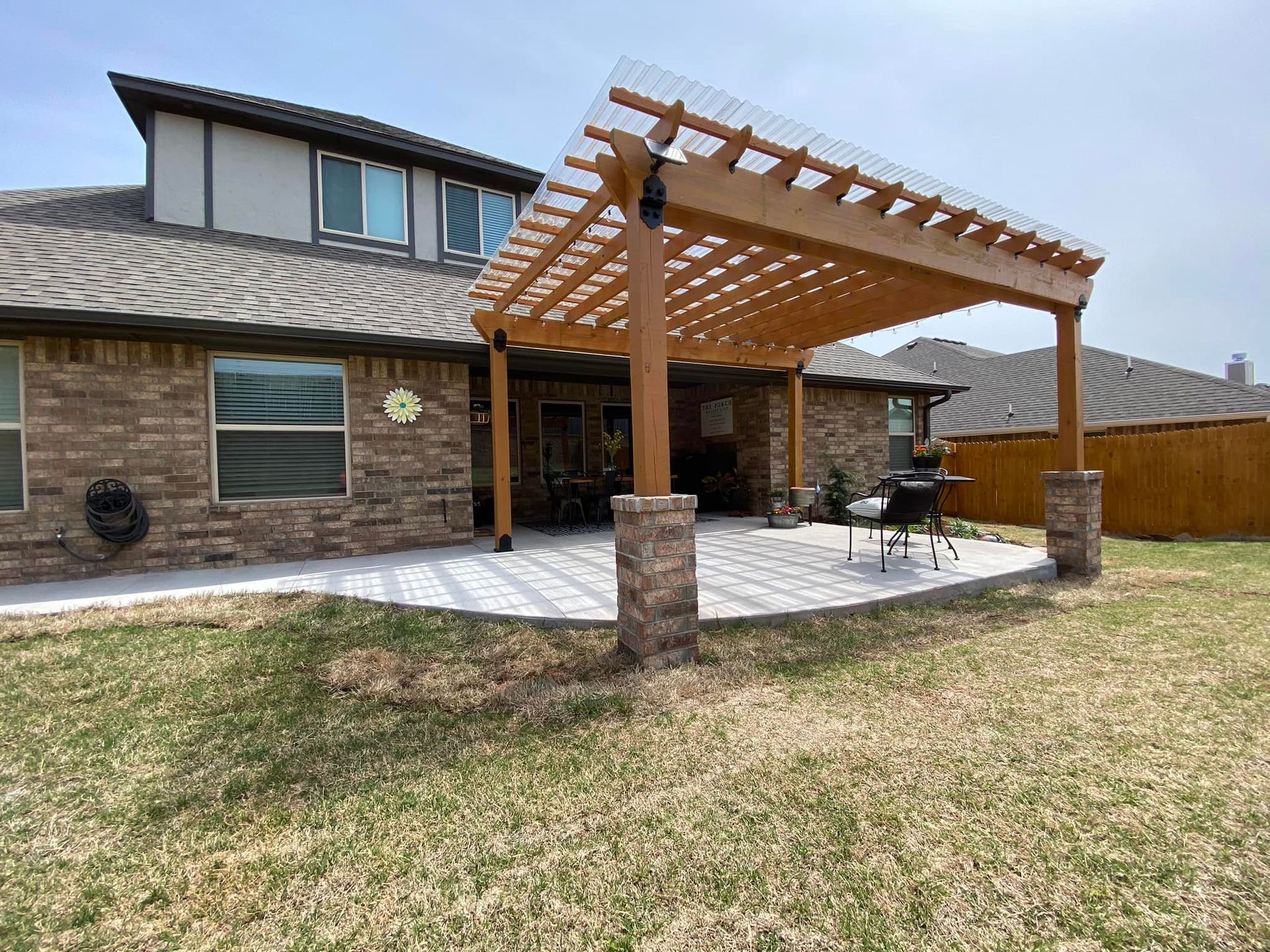 Backyard patio with brick home, wooden pergola, and stone columns.