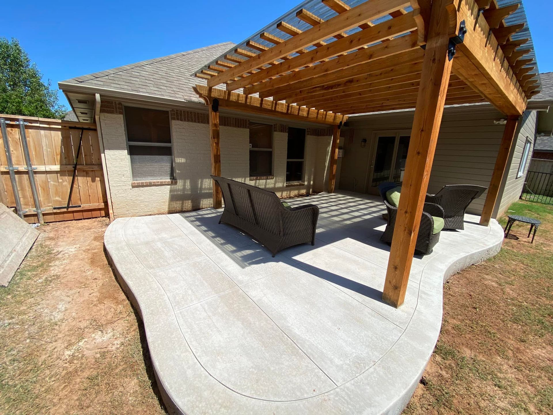 Concrete patio with a wooden pergola and furniture in a backyard.