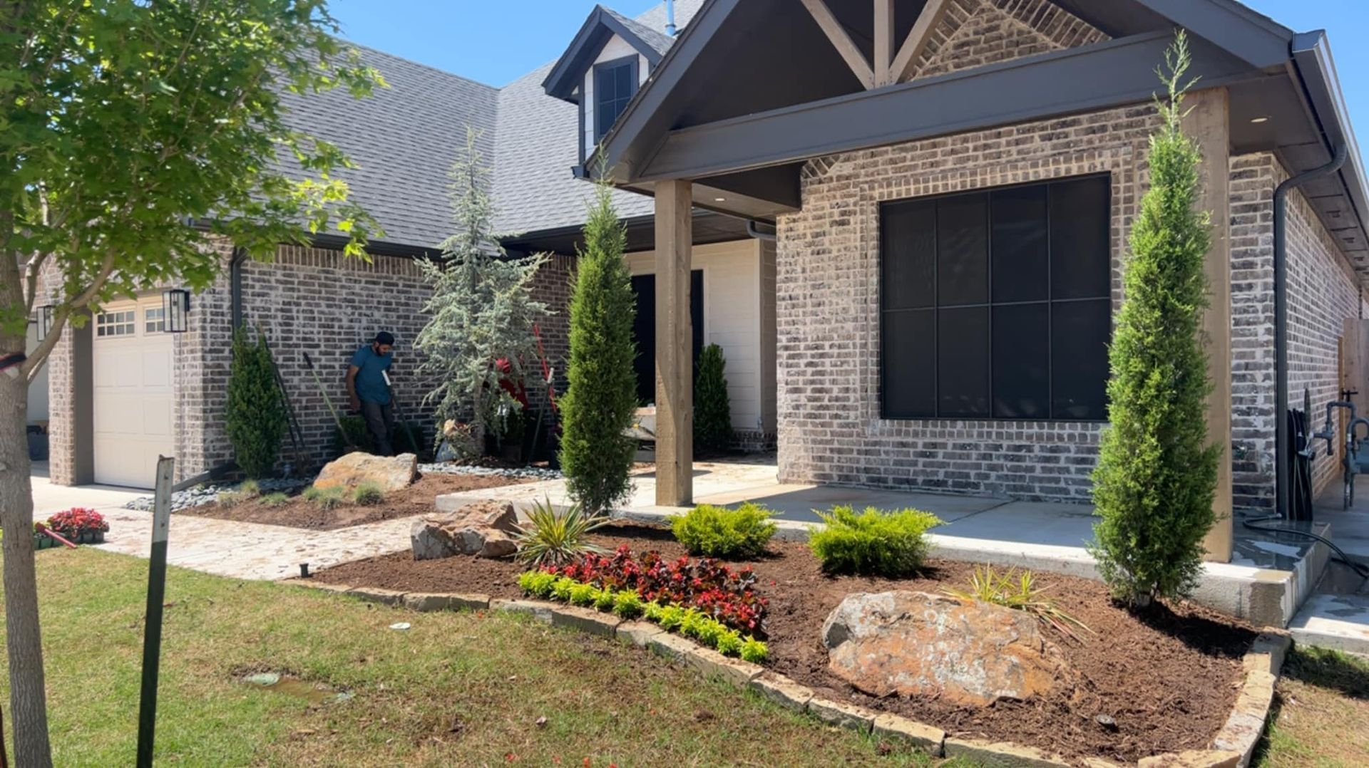 A house with brick facade, well-maintained landscaping, and a person working on the lawn.