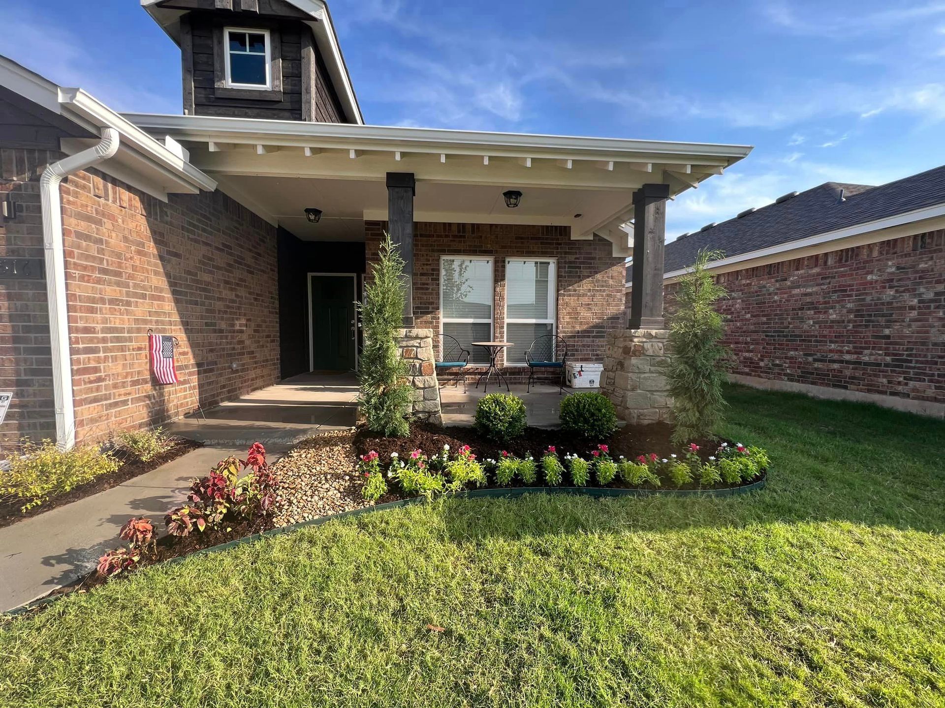 A brick house with a porch and a lawn in front of it.
