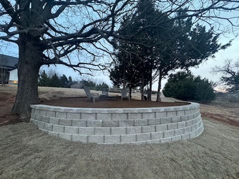 Retaining wall with seating area under a large tree, brown mulch, gray blocks, and green grass.