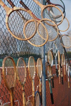 Langs een gaashekwerk op een gravelbaan hangen talloze vintage houten tennisrackets.