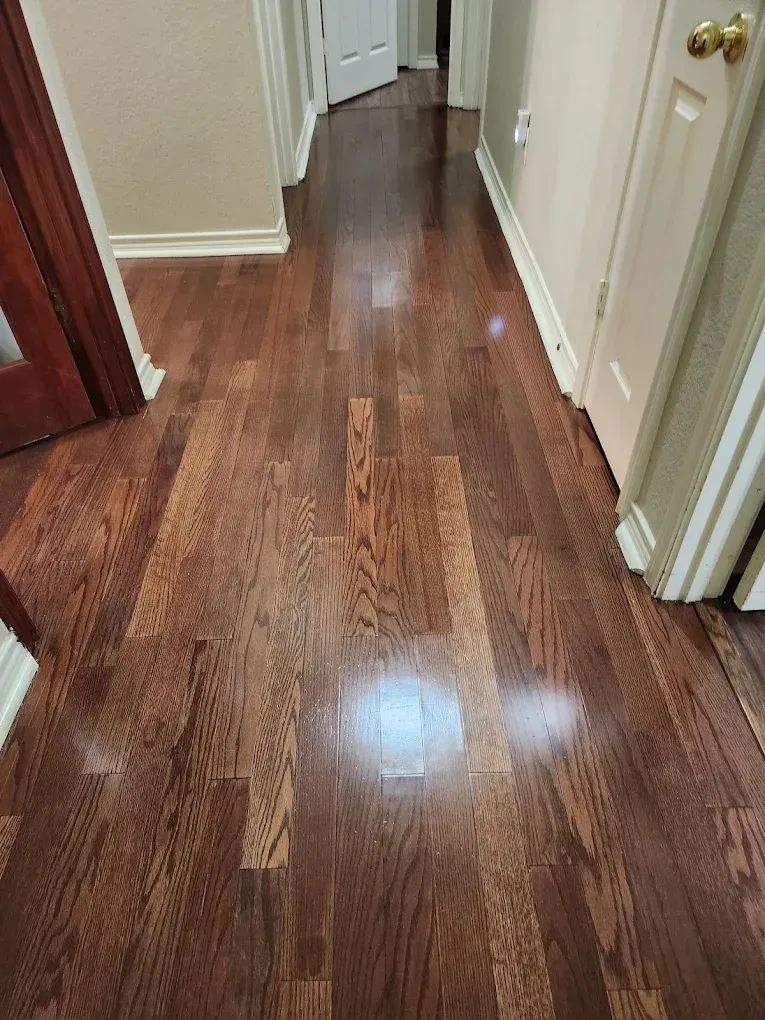 Dark-stained hardwood floor in a hallway with white trim, leading towards a closed white door.
