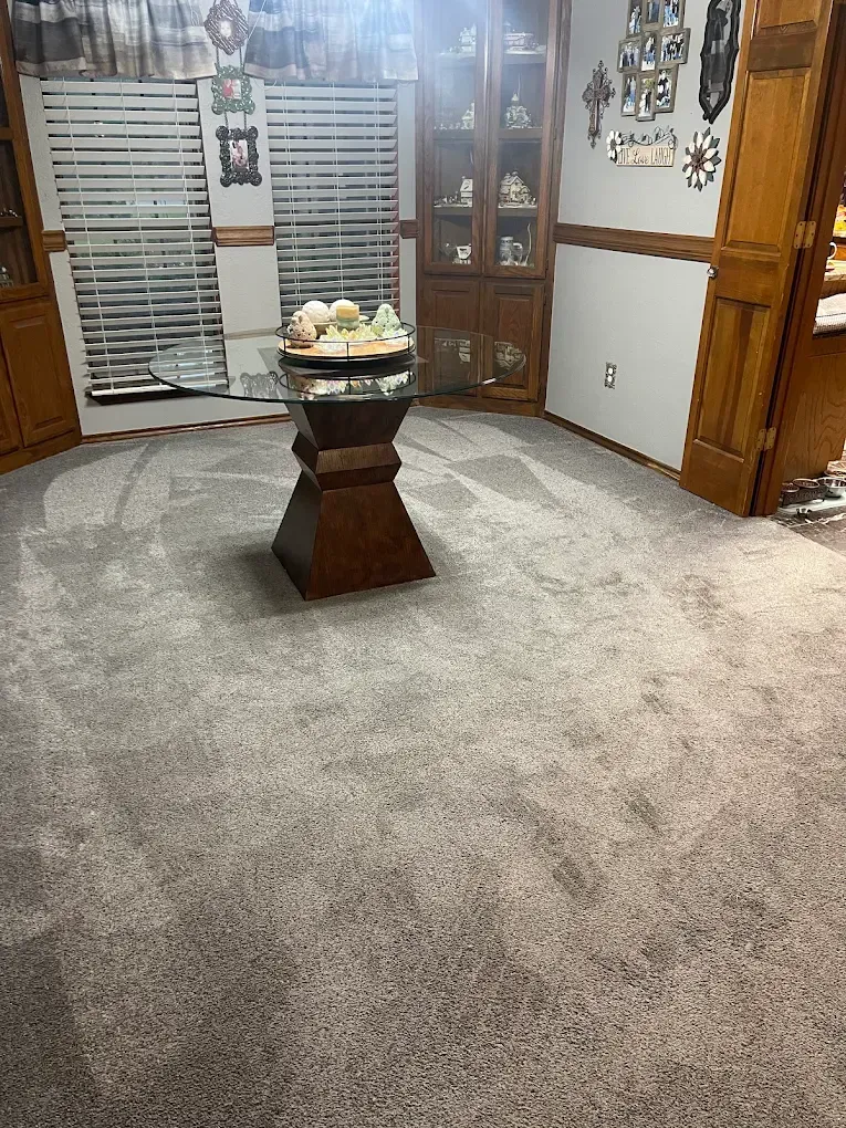 Dining room with grey carpet, wooden accents, and a central pedestal table with decorative items.