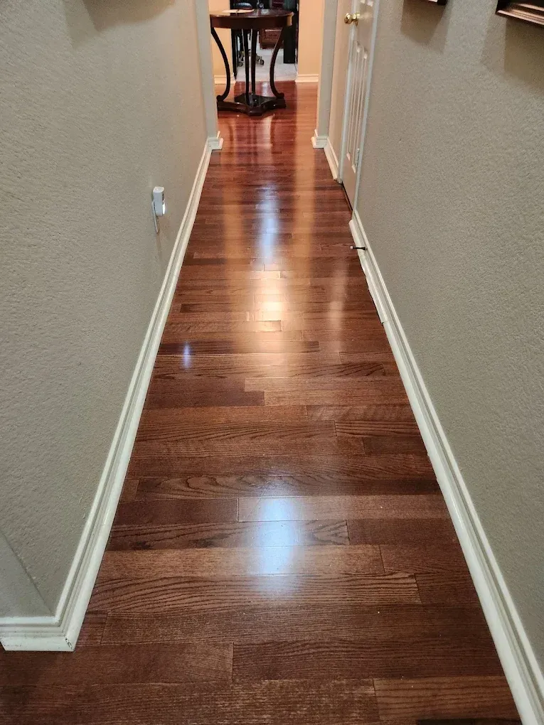 Hallway with shiny, dark wood floor, beige walls, and white trim.