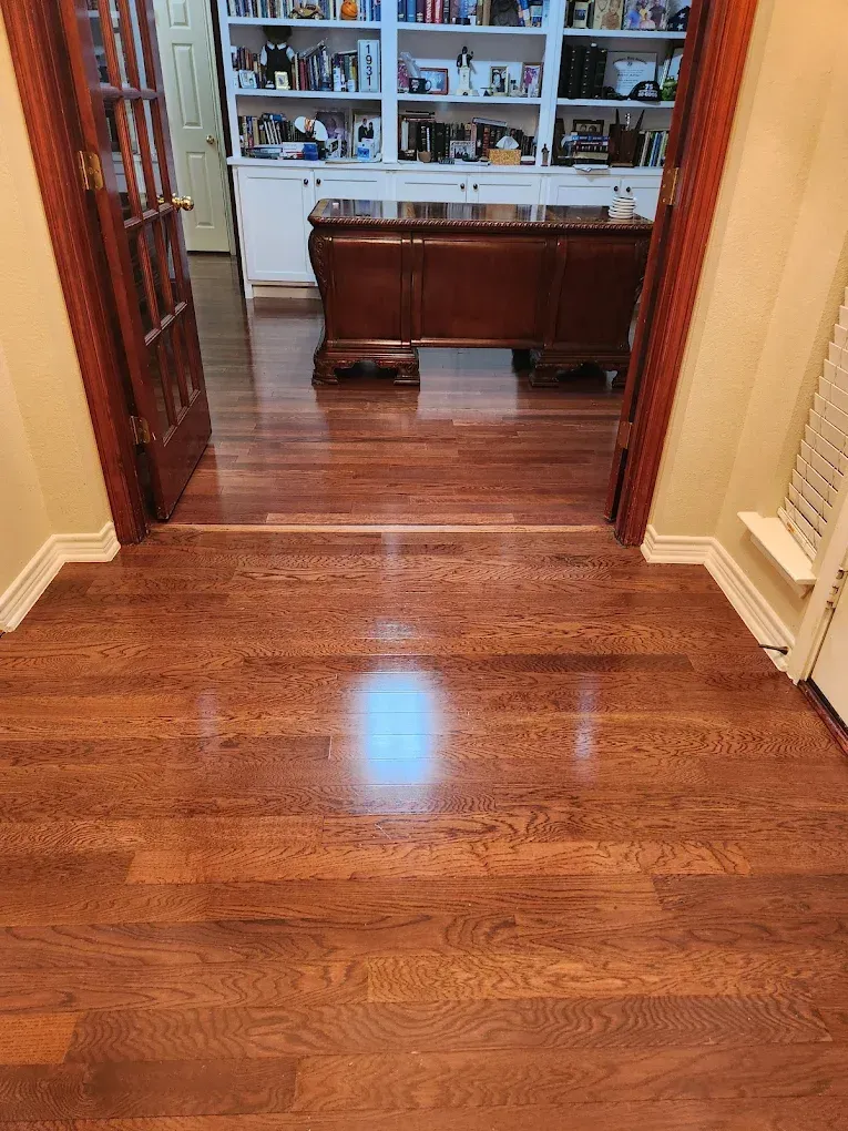 Hardwood floor leads to a room with a large desk and bookshelves.