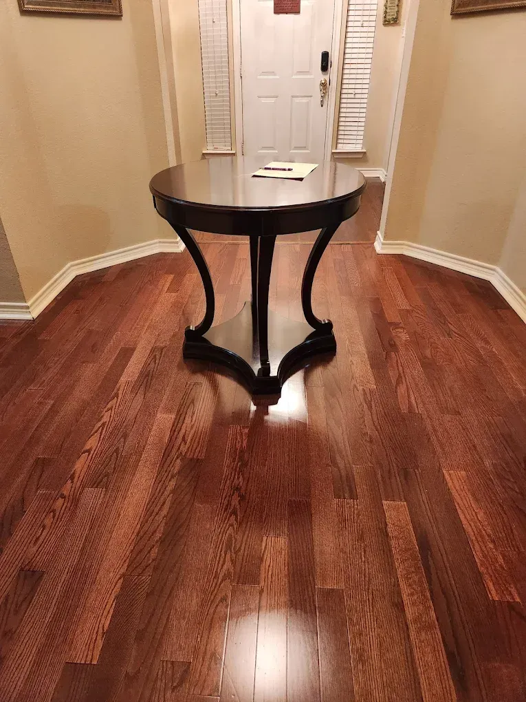 Dark wooden table in a hallway with hardwood floors, beige walls, and a white door in the distance.