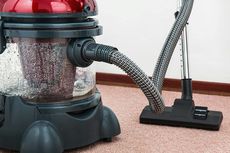 Wet-dry vacuum cleaner with a red top, black hose, and nozzle on a pink rug.