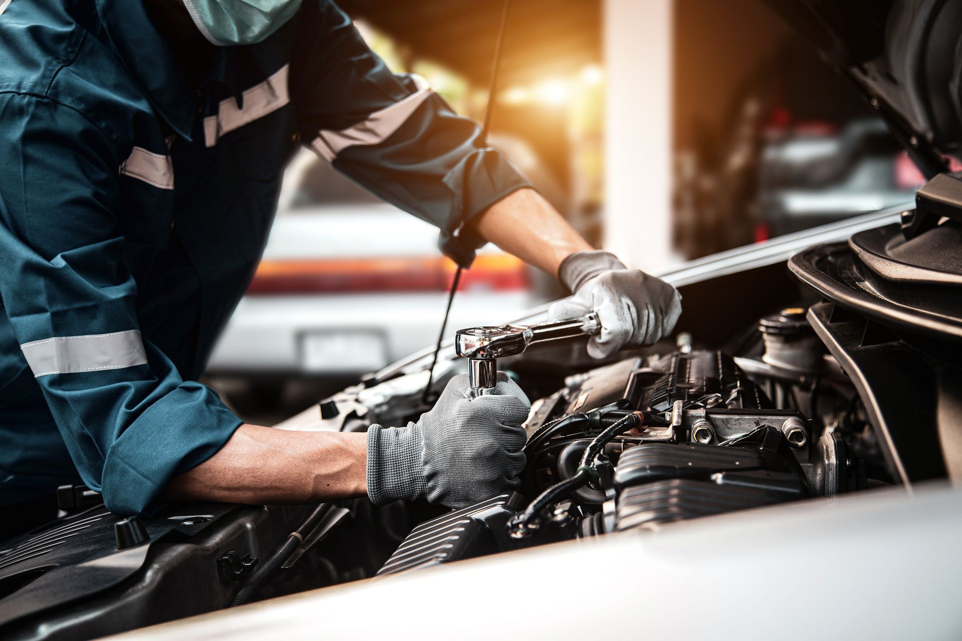 A man wearing a mask is working on the engine of a car.