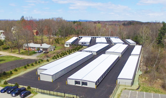 Aerial view of a storage facility with several long, white buildings and a black asphalt parking area.