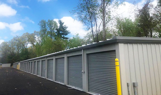Row of gray storage units under a bright blue sky with trees in the background.