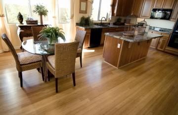 Bright kitchen with wood floors, island, round table, and wicker chairs near sunlit windows.