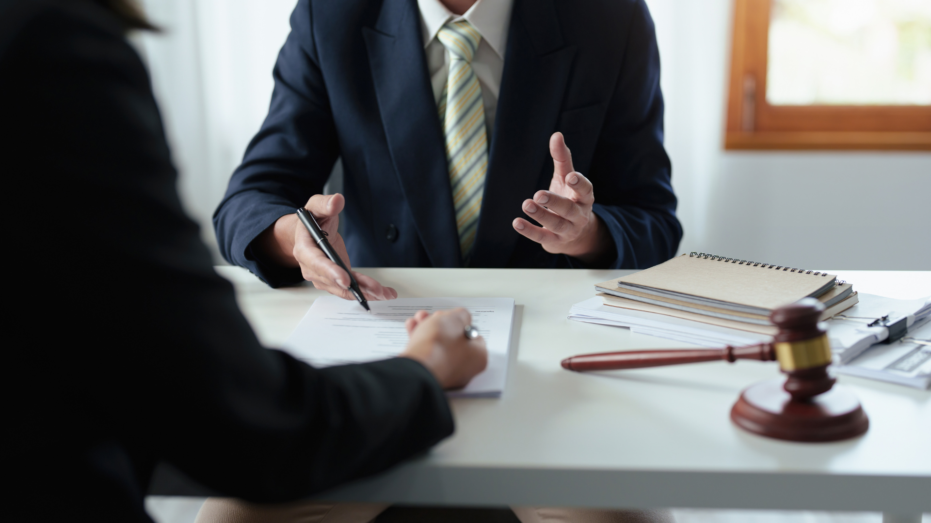 Two people sit at a table reviewing documents, with a wooden gavel resting nearby in an office setting.