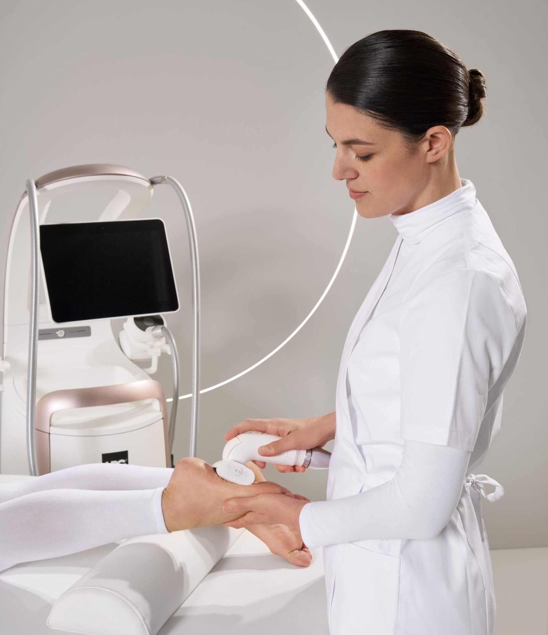 Een vrouw in een witte jas gebruikt een machine op de arm van een patiënt.