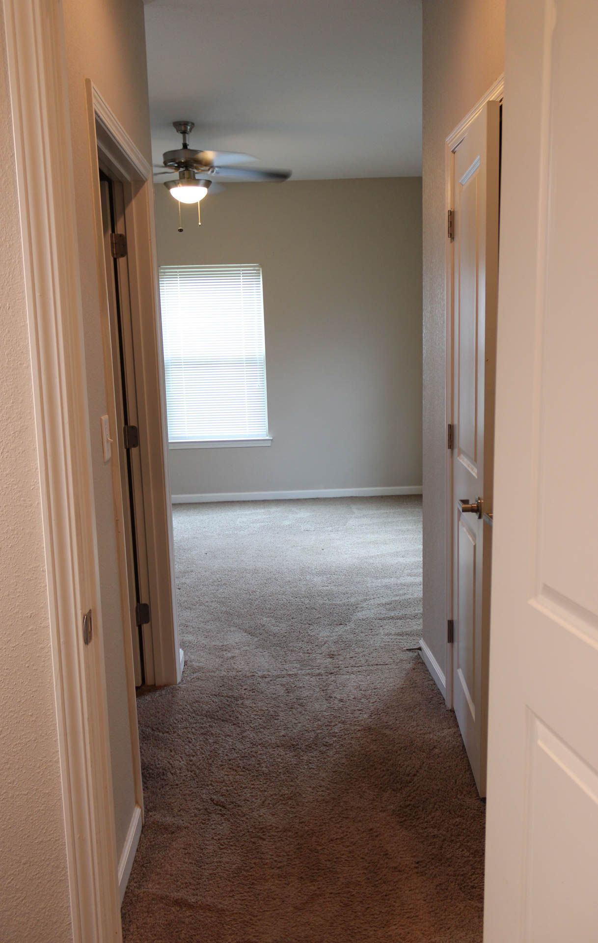 A hallway in a house with a ceiling fan and a window.