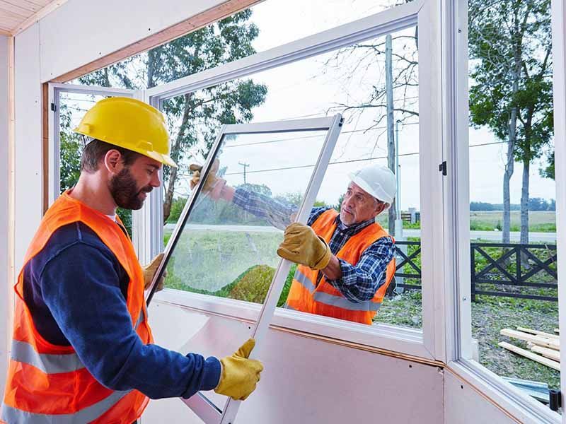 Two men are installing a window in a house.
