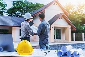 Two construction workers are looking at a blueprint in front of a house under construction.