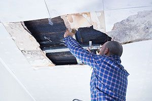 A man is standing on a ladder fixing a hole in the ceiling.