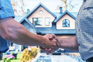 Two men are shaking hands in front of a house.