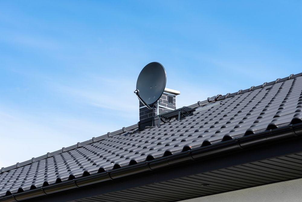 Satellite dish on a gray tiled roof against a blue sky — MATV Systems Australia Pty Ltd in Wickham, NSW