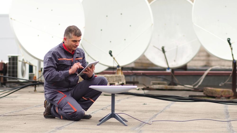 Technician Inspecting a Tablet Beside Large White Satellite Dishes — MATV Systems Australia Pty Ltd in Wickham, NSW