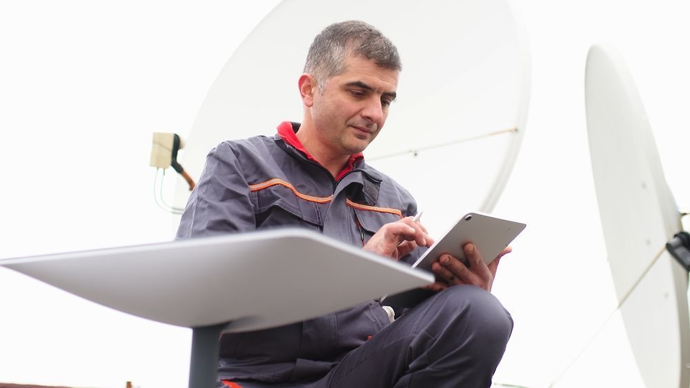 Technician Using a Tablet Beside Satellite Dishes Outdoors — MATV Systems Australia Pty Ltd in Wickham, NSW