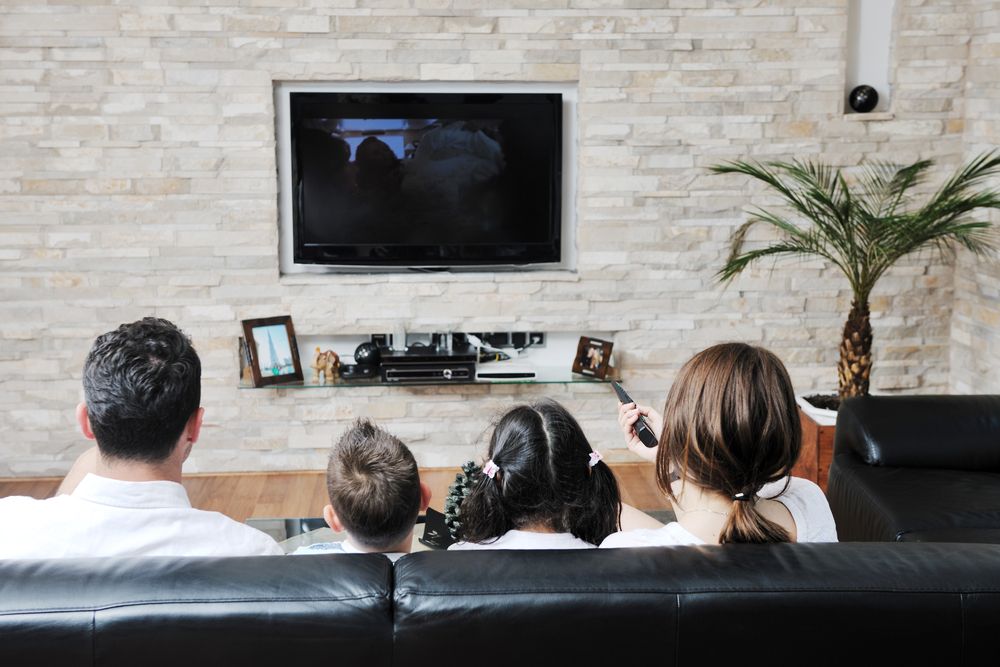 Family Seated on a Couch Watching TV in a Modern Living Room — MATV Systems Australia Pty Ltd in Wickham, NSW