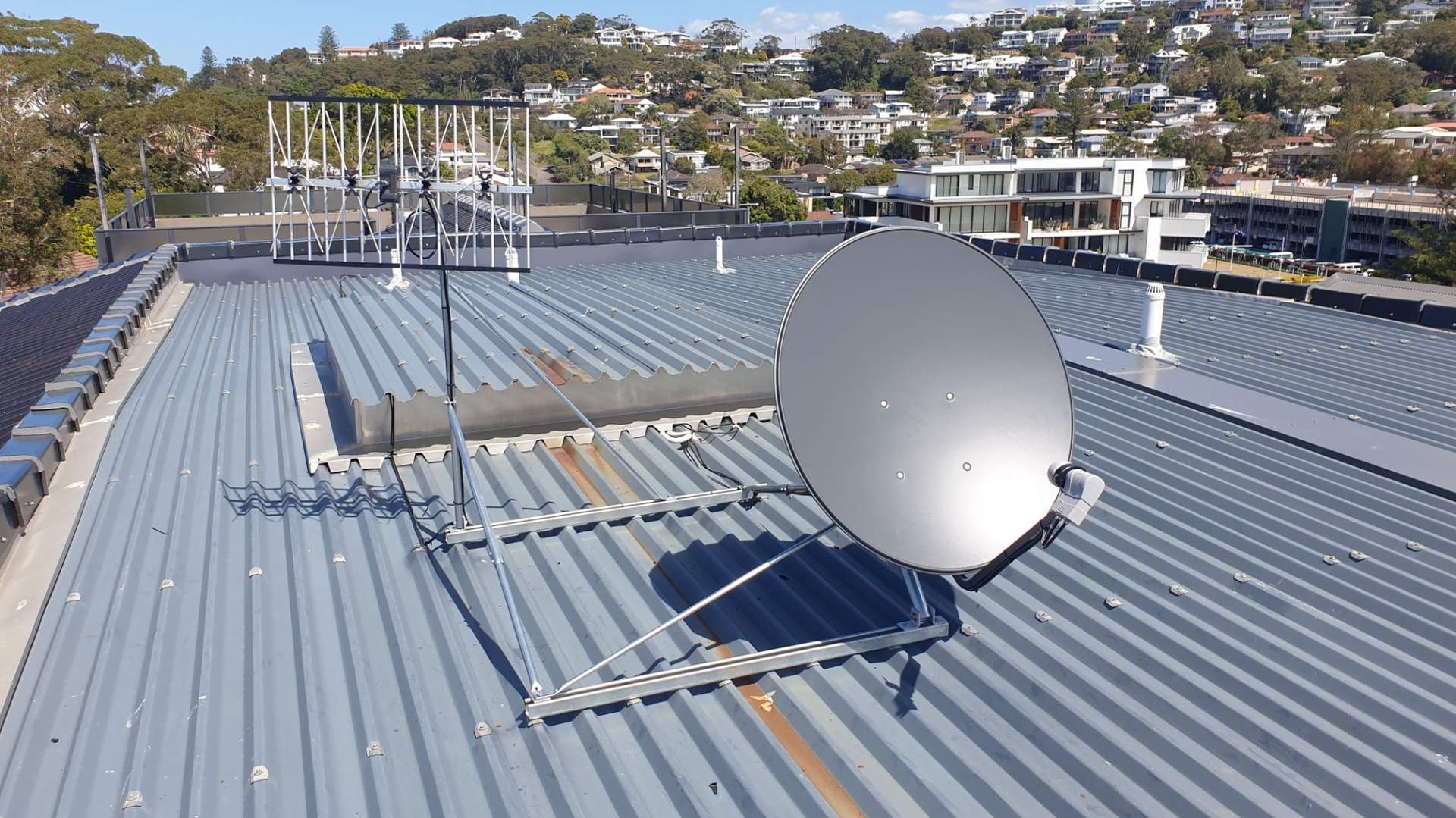 Satellite dish on a corrugated metal roof with antennas and buildings in the background.