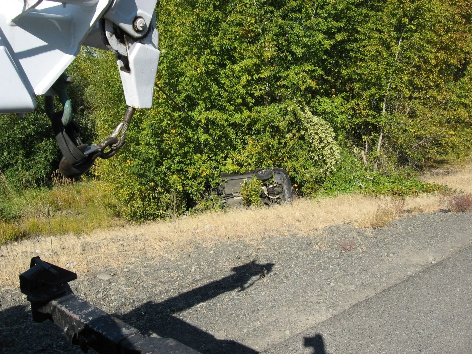 Tow truck preparing to remove a car that has crashed off the side of the road, nestled in bushes.