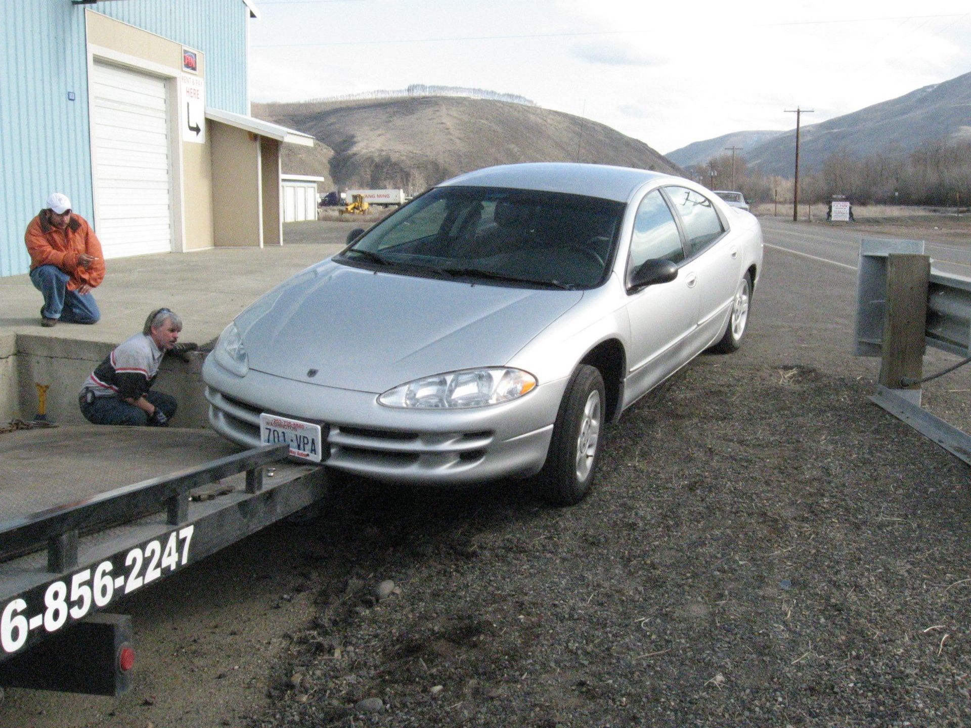 A silver car is being towed by a tow truck