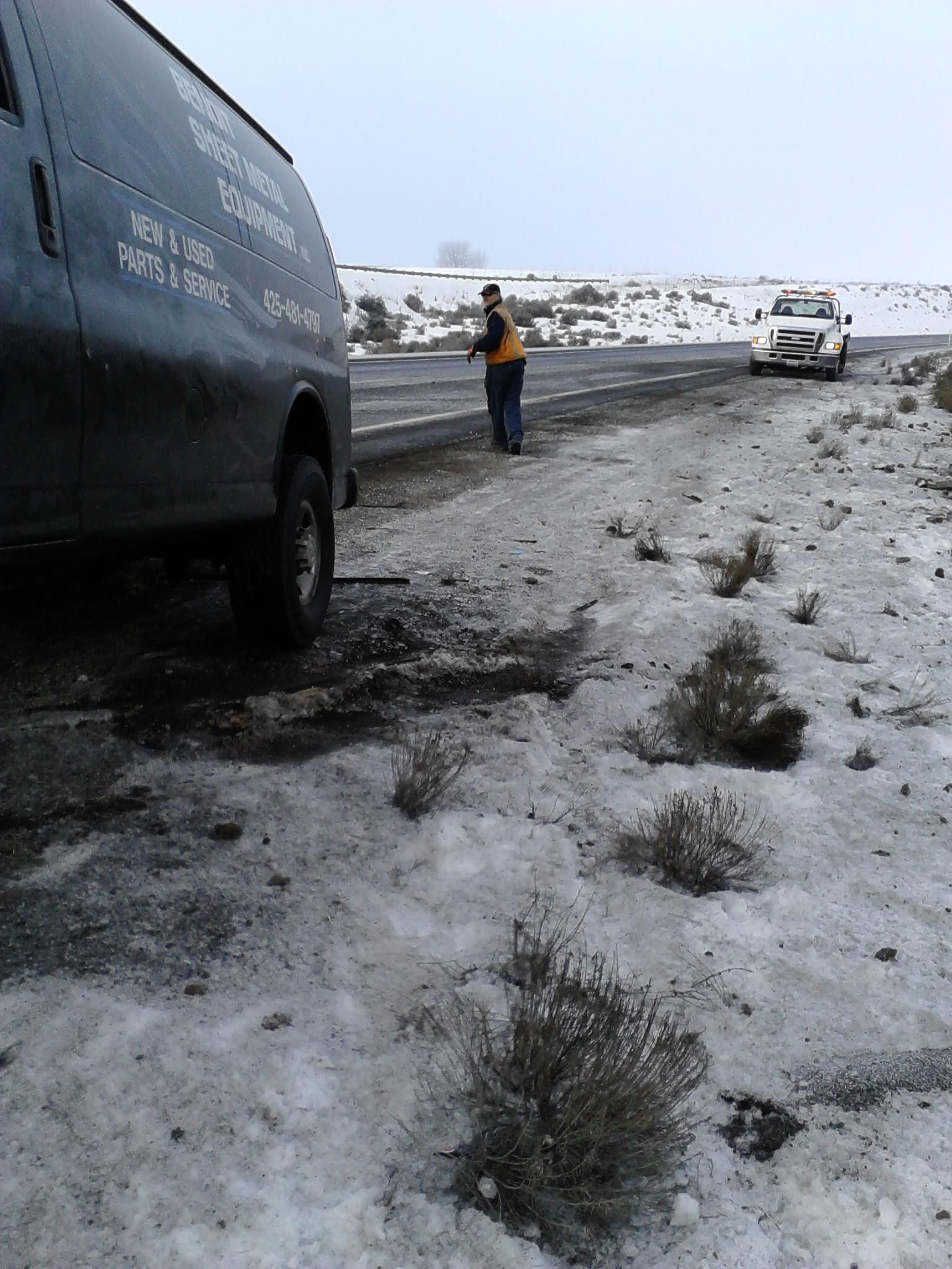 A man is standing next to a black van in the snow.