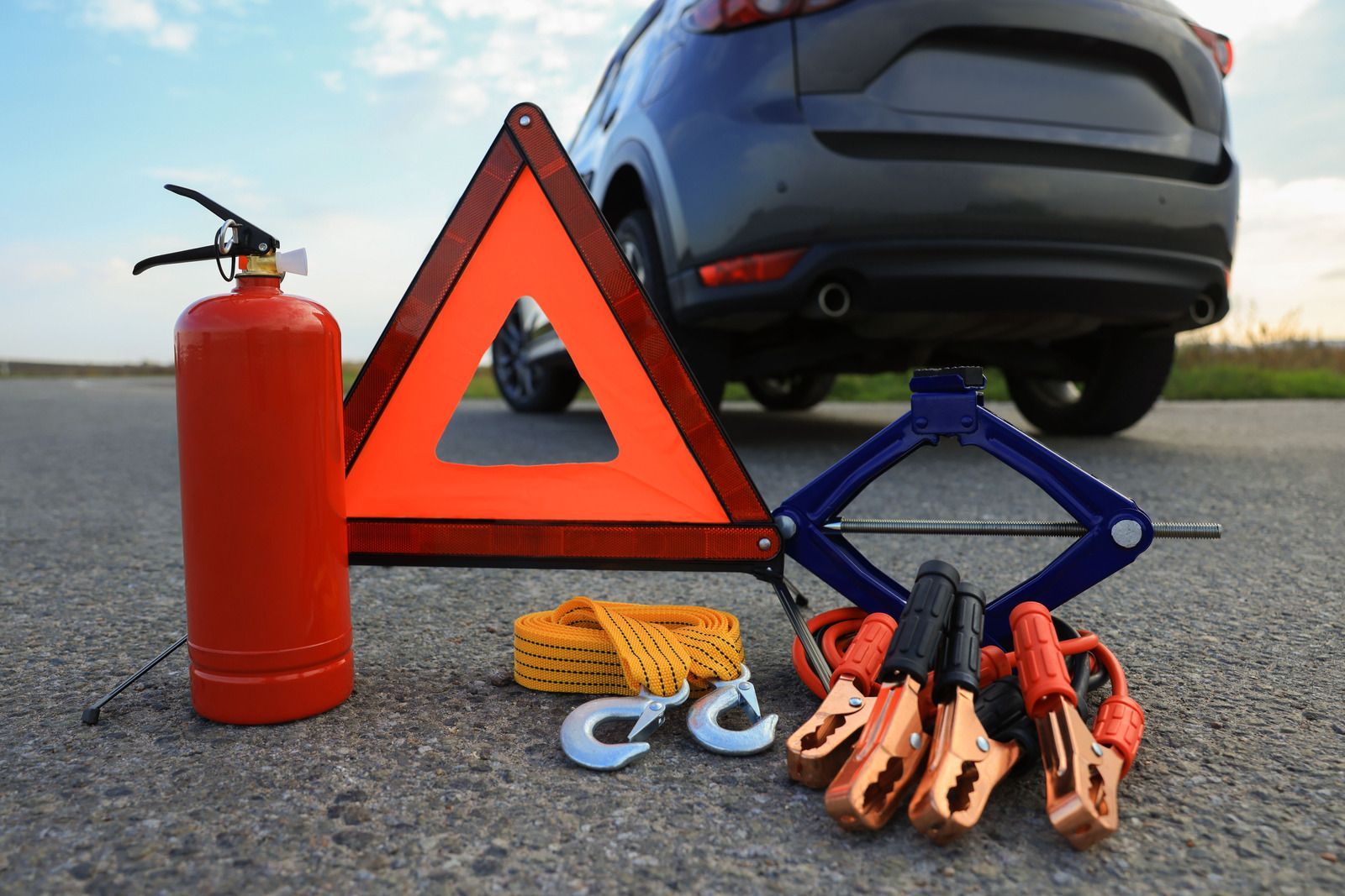 A car is sitting on the side of the road next to a fire extinguisher and a warning triangle.