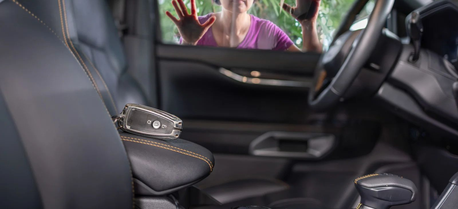 Keys on car armrest with person locked out looking in.
