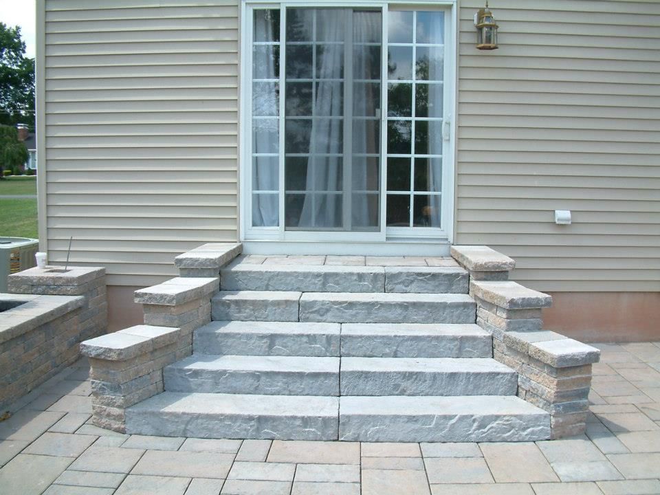 Stone steps with matching short pillars leading to a sliding glass patio door on a house with beige siding.