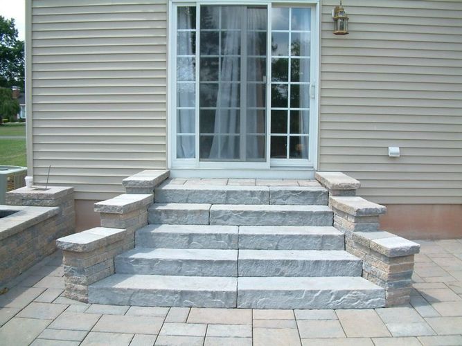 Stone steps with matching short pillars leading to a sliding glass patio door on a house with beige siding. Stone steps with matching short pillars leading to a sliding glass patio door on a house with beige siding.