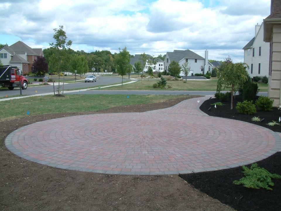 A circular stone paver patio surrounded by fresh soil and landscaping in a suburban residential neighborhood.