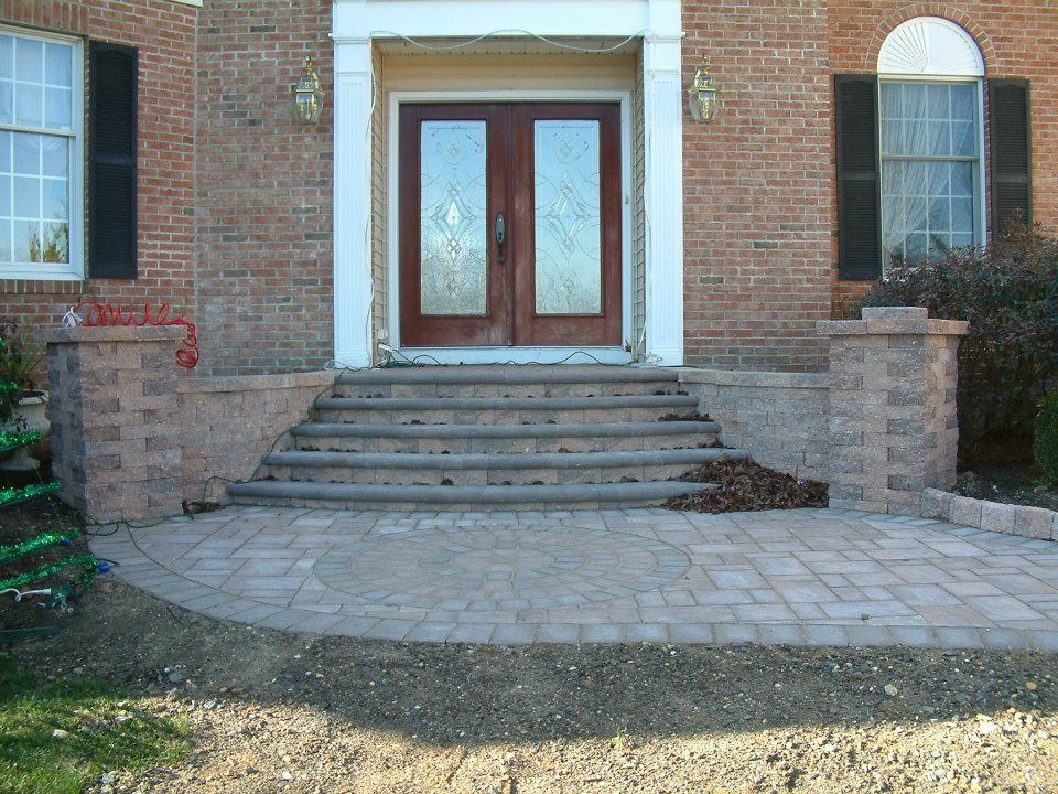 Brick home entrance featuring stone stairs, a paved circular walkway, and pillars flanking the front double doors. Brick home entrance featuring stone stairs, a paved circular walkway, and pillars flanking the front double doors.