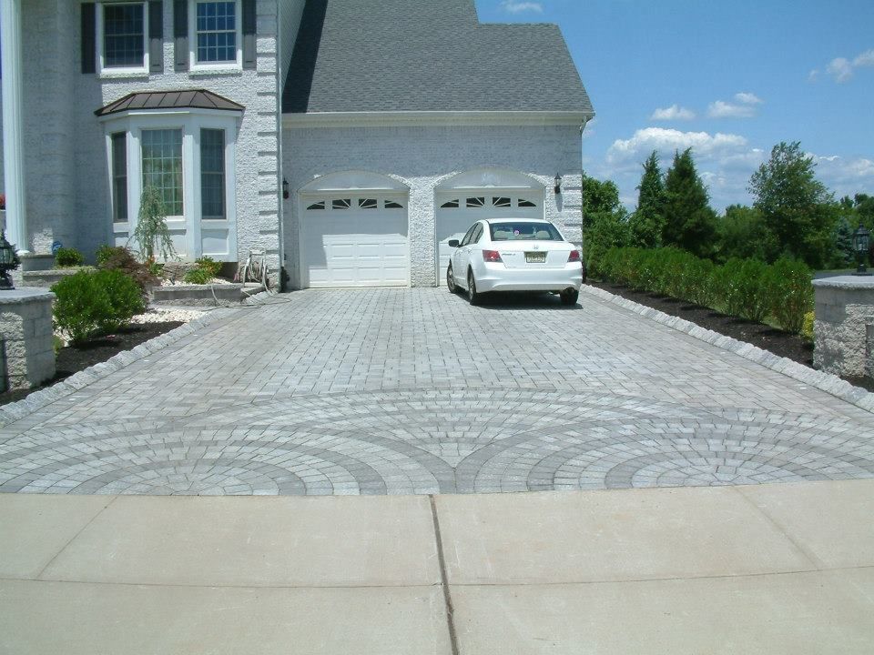 A white house with a patterned paver driveway featuring a circular design, with a white car parked in front of the garage.