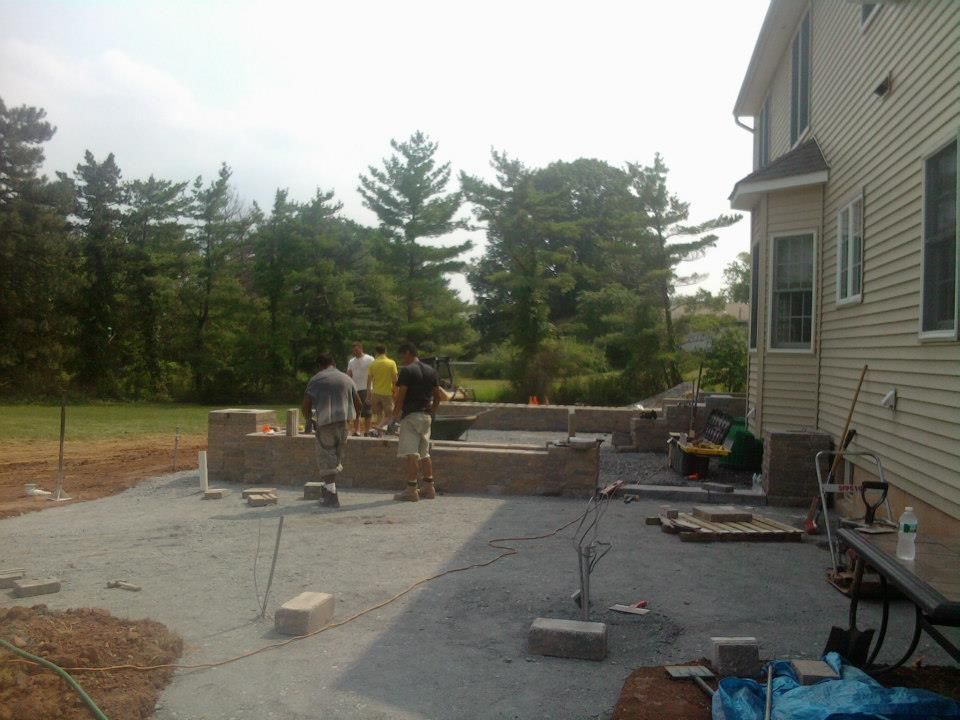 Four workers build a stone patio wall in the backyard of a residential home.