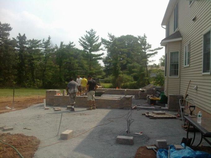 Four workers build a stone patio wall in the backyard of a residential home. Four workers build a stone patio wall in the backyard of a residential home.