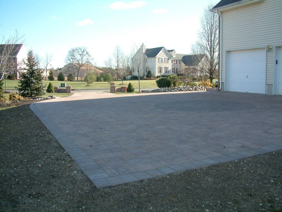 A paved driveway made of grey stone bricks in front of a house with a white garage door, set in a suburban neighborhood. A paved driveway made of grey stone bricks in front of a house with a white garage door, set in a suburban neighborhood.