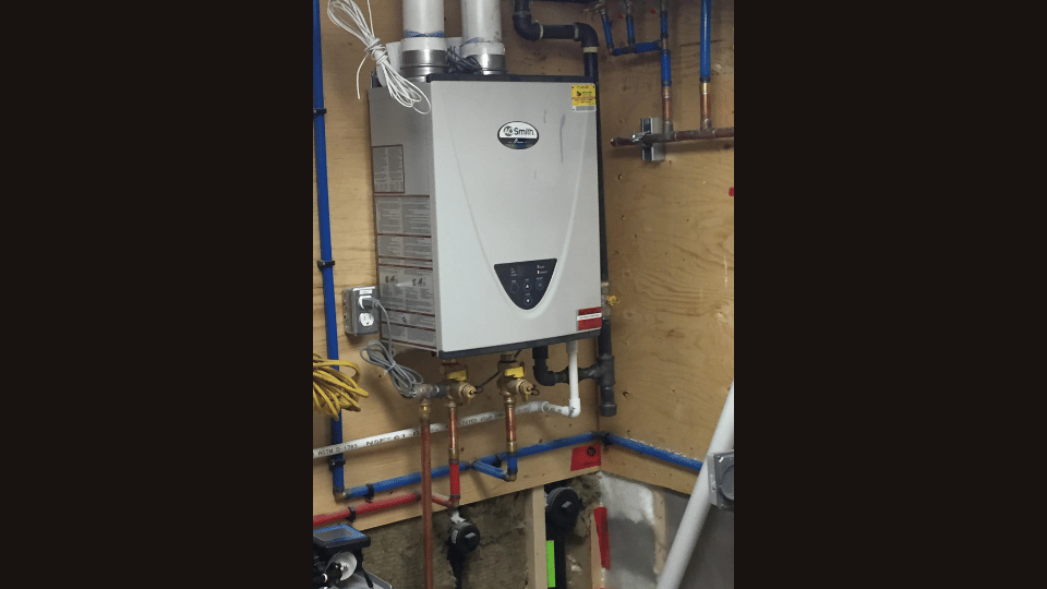 A water heater is hanging on a wall next to pipes.