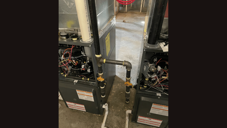 Two air conditioners are sitting next to each other in a basement.