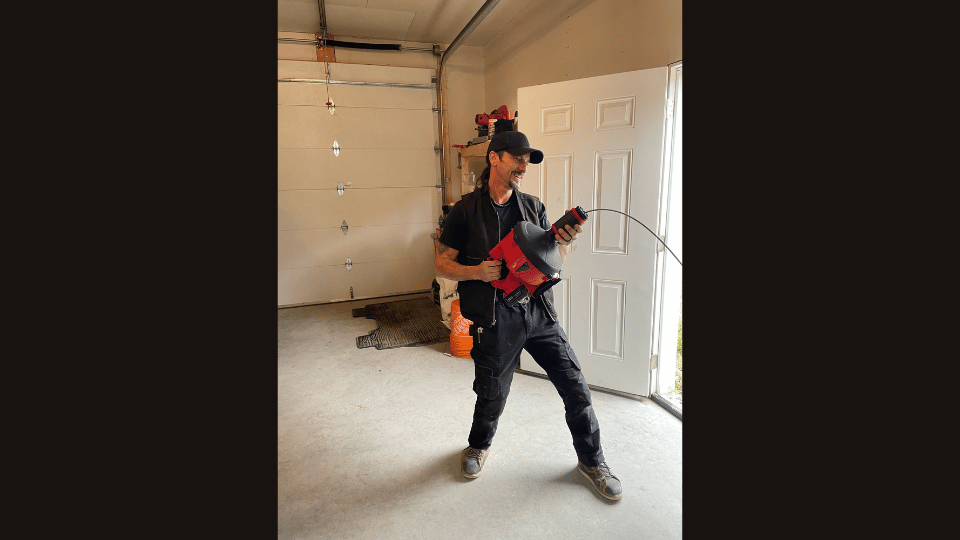 A man is standing in a garage holding a drill.