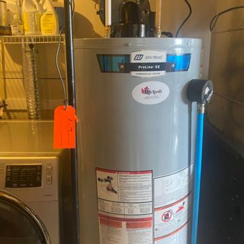 A water heater is sitting in a laundry room next to a washer and dryer.