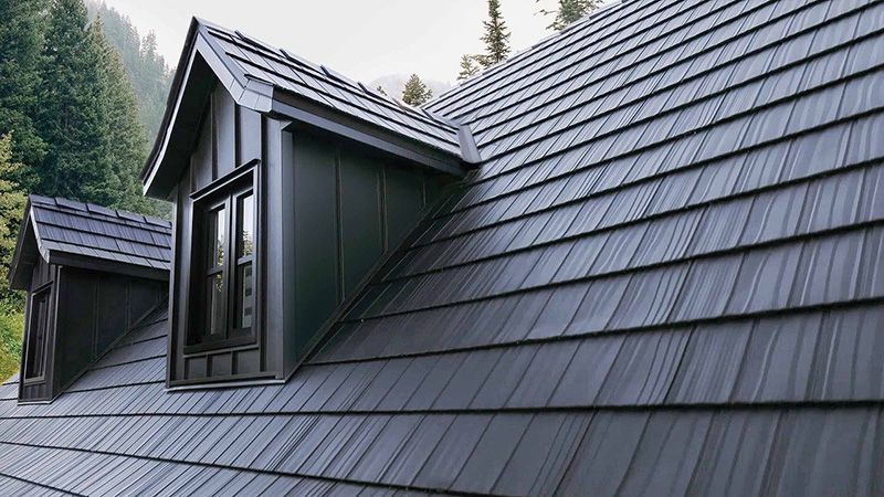 Toiture en métal gris foncé avec lucarnes sur fond de montagne.