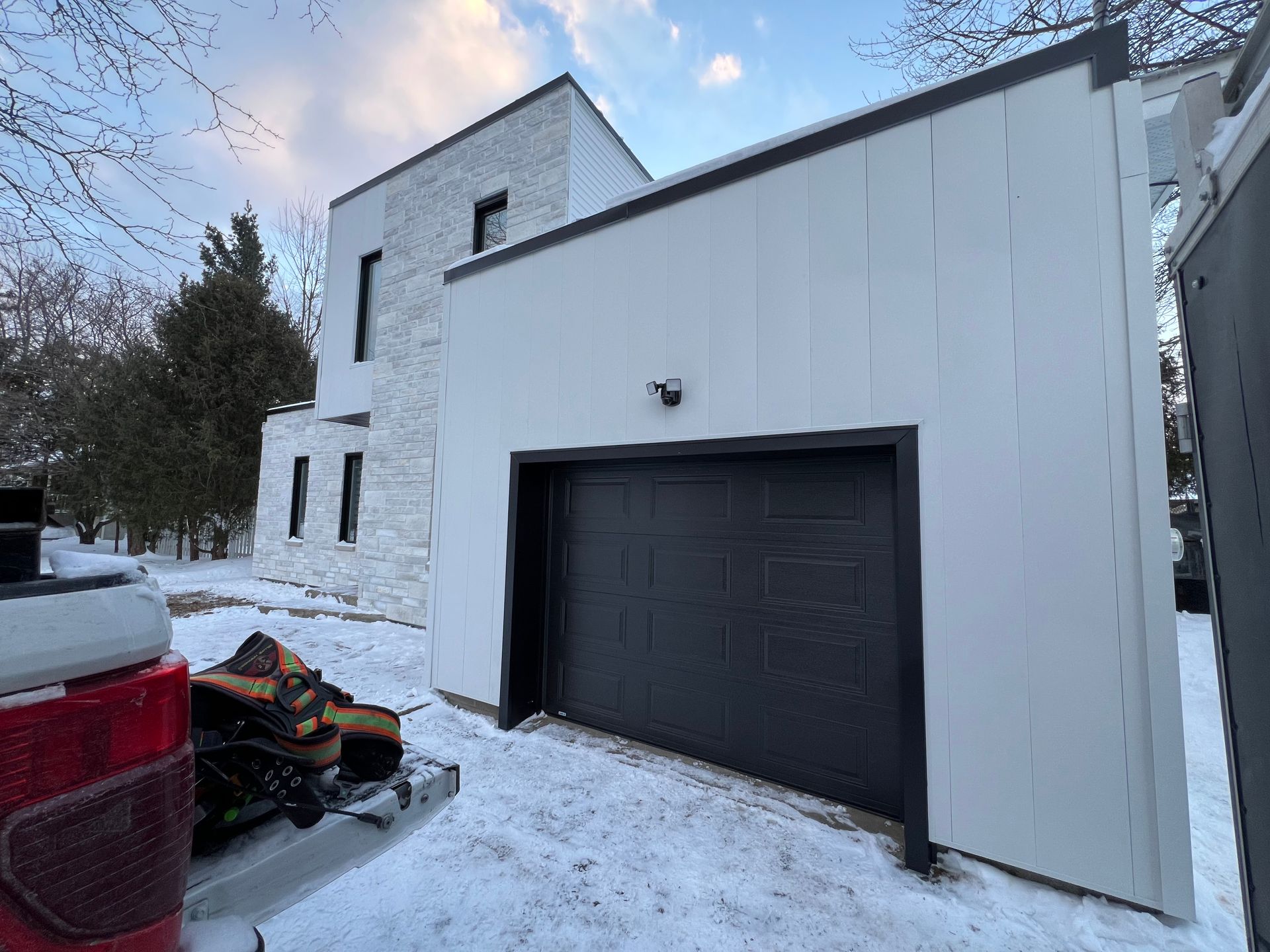 Un camion rouge est garé devant une maison blanche avec une porte de garage noire.