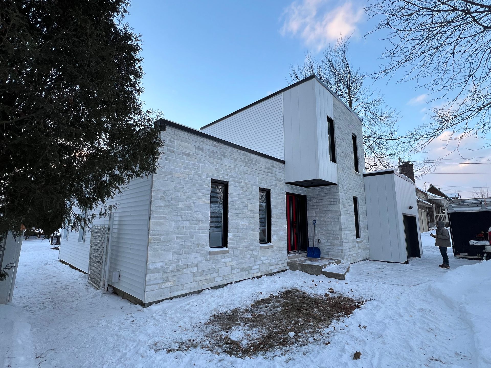 Une maison blanche avec une porte rouge est couverte de neige