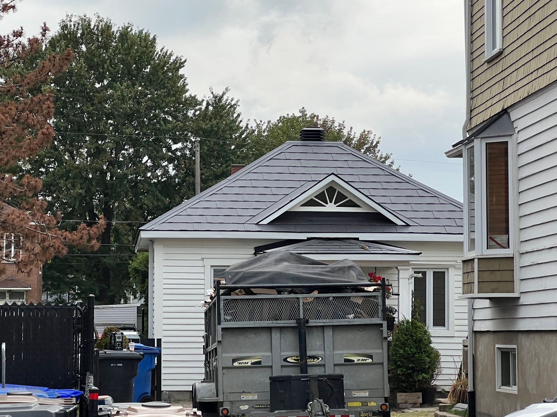 Une benne à ordures est garée devant une maison au toit d'ardoise.